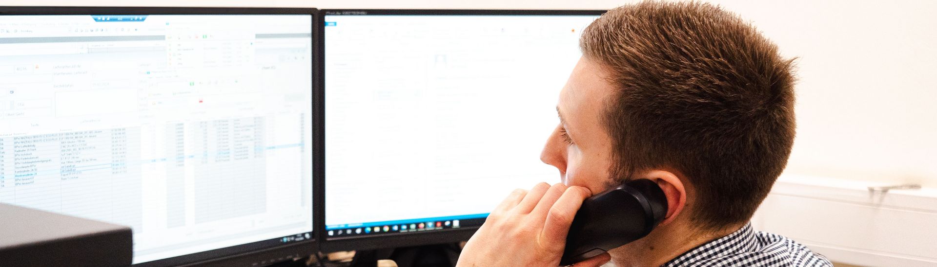 Servicemitarbeiter telefoniert und schaut auf zwei Monitore